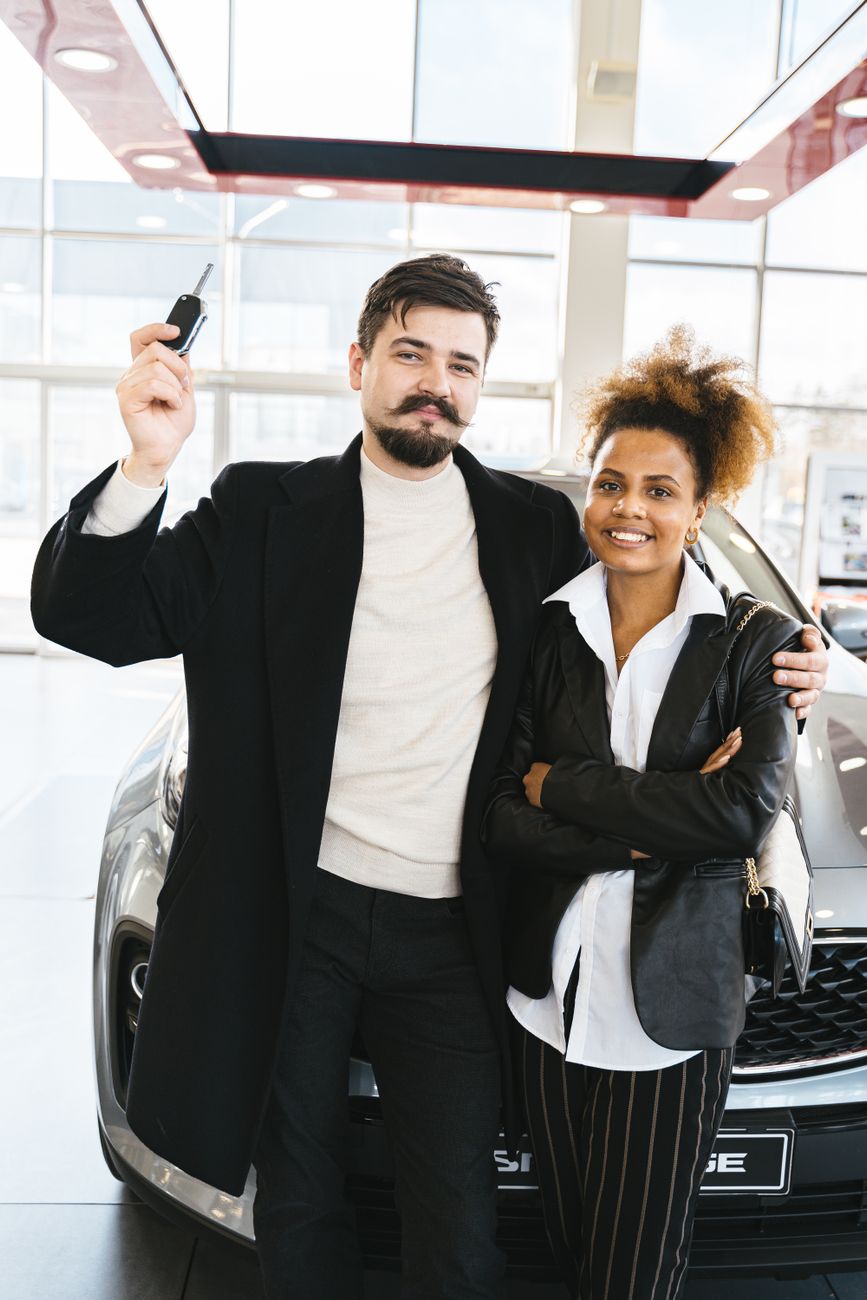 Couple holding up a car key fob in a dealership showroom